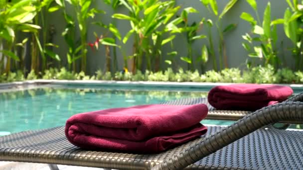 Close-up de toalhas vermelhas em espreguiçadeiras perto da piscina azul no dia quente do verão — Vídeo de Stock