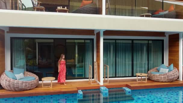 Молода красива жінка виходить з готелю прямо в блакитний плавальний басейн — стокове відео