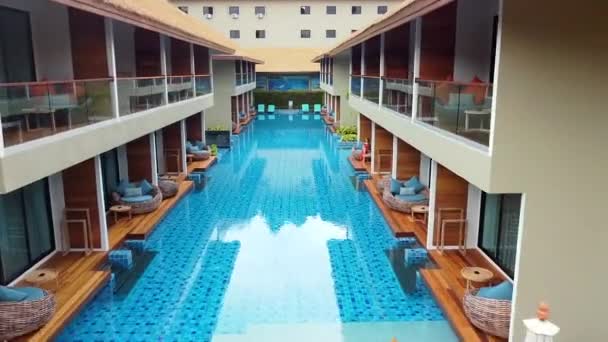 Dron latający nad niebieskim basenem w luksusowym kurorcie pomiędzy budynkiem z dwoma piętrami — Wideo stockowe