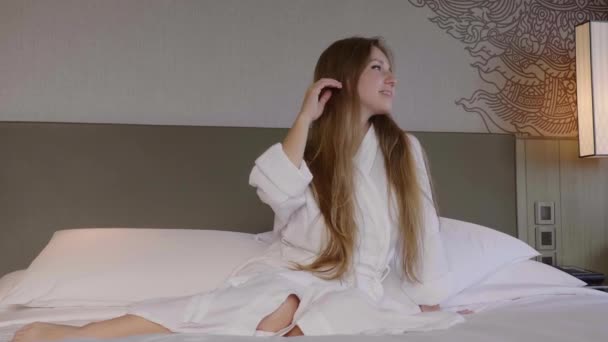 Mujer hermosa joven en blanco Albornoz Relajante en la cama en el hotel, Sonriendo — Vídeo de stock