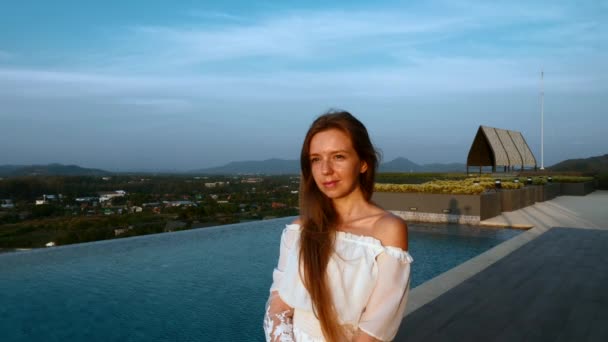 Νεαρή χαμογελαστή γυναίκα στέκεται στην ταράτσα με πισίνα και να απολαύσετε το ηλιοβασίλεμα — Αρχείο Βίντεο