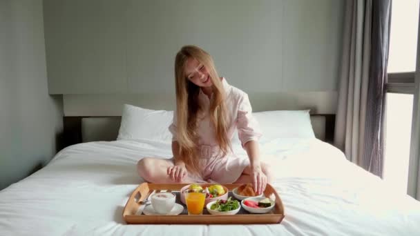 Счастливая кузнечица ест круассан на завтрак в постели в современном отеле — стоковое видео
