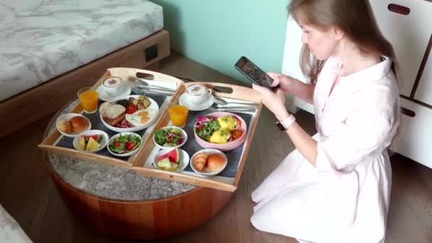 Блогер Женщина сделать фотографии завтрака в номере отеля, используя мобильный телефон — стоковое видео