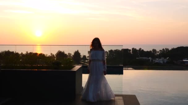 Femme en robe blanche marchant seule sur le toit de l'hôtel avec vue sur le coucher de soleil rose — Video