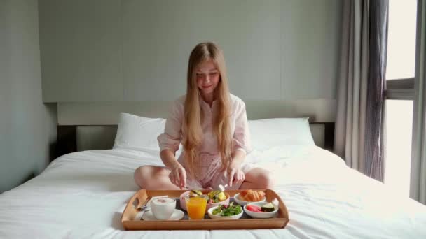 Πρωινό στο κρεβάτι - Ευτυχισμένη γυναίκα κάθεται στο κρεβάτι στο ξενοδοχείο, πίνοντας καφέ — Αρχείο Βίντεο