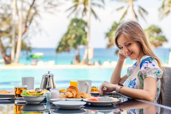 リゾートレストラン、プール、ターコイズブルーの海で朝食を食べる若い女性背景 — ストック写真