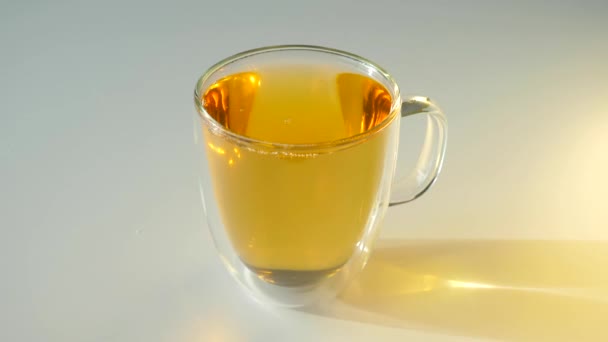 Copa de vidrio con té verde de pie en la mesa blanca durante el atardecer o la salida del sol — Vídeos de Stock