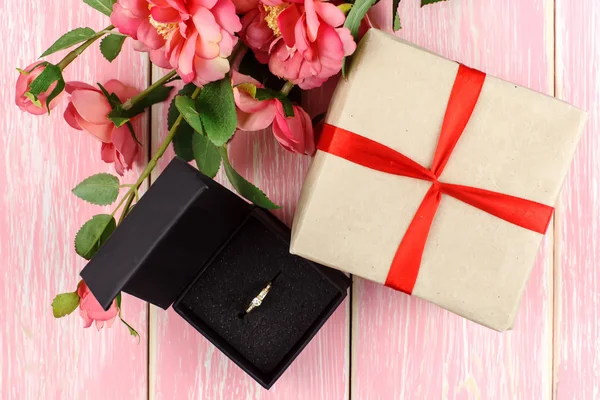 Dárek s červenou mašlí, ring v krabici a růžové květy. Selektivní zaměření. — Stock fotografie