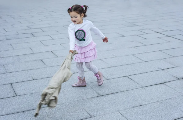 Happy tří letá dívka si hraje s kabát ve městě — Stock fotografie