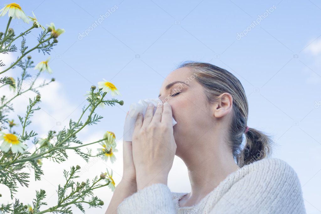 Woman sneezing in a daisy flowers meadow