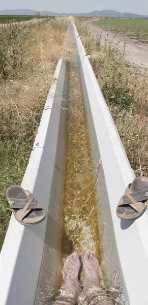 Pies de hombre refrescantes en un canal de riego fresco —  Fotos de Stock