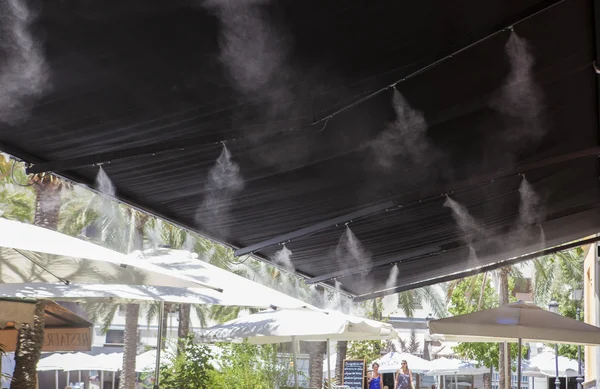 Разбрызгиватели навеса брызгают водой в баре на террасе — стоковое фото