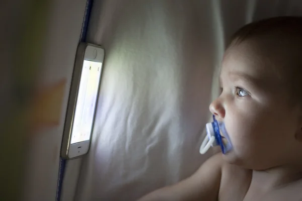 Bebek beşik üstünde hareket eden telefon ile bir ninni çizgi film izlerken — Stok fotoğraf