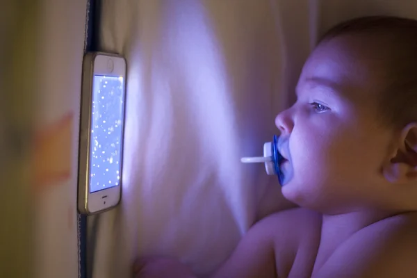 Bebé viendo una canción de cuna de dibujos animados con teléfono móvil en la cuna — Foto de Stock