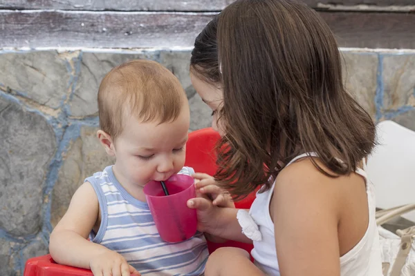 Sorellina che aiuta il suo fratellino a bere — Foto Stock