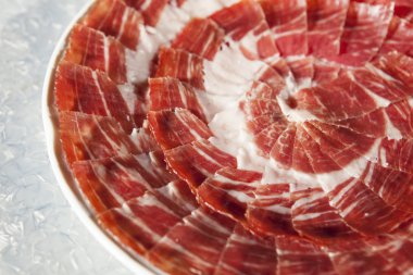 Circular decorative arrangement of iberian cured ham on plate clipart