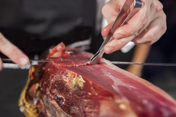 Master slicer taking iberian cured ham with tongs — Stock Photo, Image