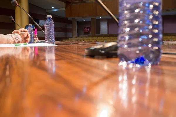 Crossed hand of speaker over table with no people at conference hall. Selective focus