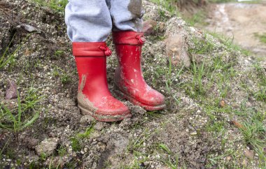 Küçük çocuk kırmızı çamurlu çizmeler giyiyor. Yağmur mevsimi ve çocuk konsepti 