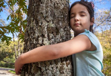 Little girl hugs tree trunk. Children love nature concept clipart