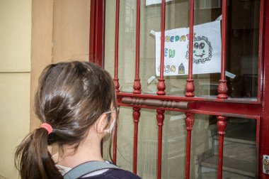 Little girl reads drawing made by children asking people to stay home during Covid confinement. Impact on children of Covid-19 confinement