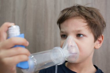 Çocuk nefes almak için tıbbi sprey kullanıyor. Astım spreyi, uzay aracı ve maske. Yan görünüm