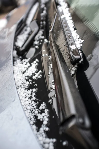 Hail falling over car wipers. Selective focus over urban background