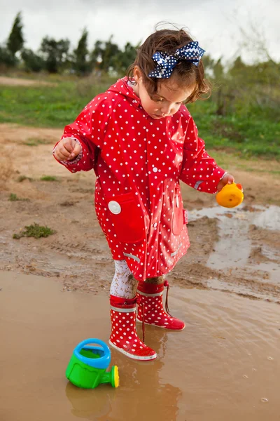 Spelen met haar water speelgoed op muddly plassen — Stockfoto