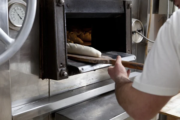 Baker sätta raw bröd i ugnen — Stockfoto