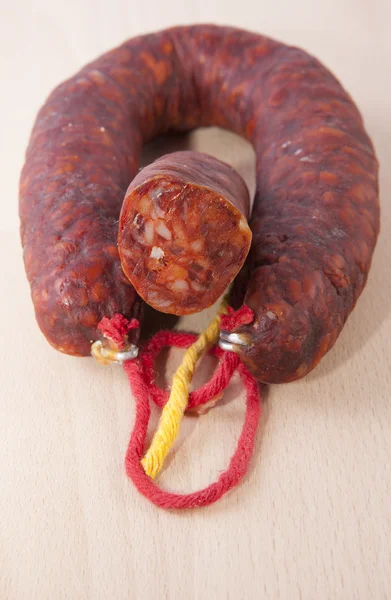 Chorizo ibérico rojo con algunas piezas cortadas sobre la superficie de madera — Foto de Stock