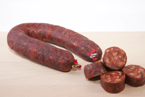 Röd Iberiska chorizo med några skär bitar över träytan — Stockfoto