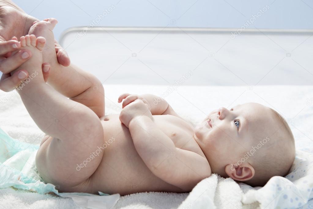 Mother holds baby legs before applying cream