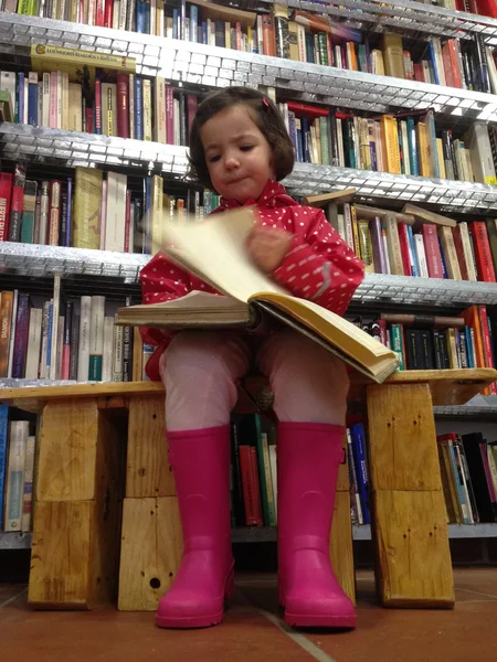 Little girl reading a thick book at bookshop — ストック写真