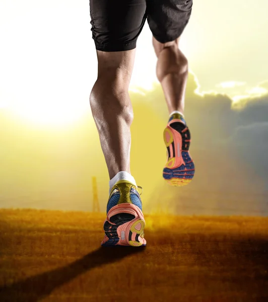 Cerrar los pies con zapatillas de correr y fuertes piernas atléticas de hombre deportivo trotando en entrenamiento de fitness entrenamiento al atardecer — Foto de Stock