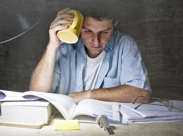 Young student at home desk reading studying at night with pile of books and coffee — Stockfoto