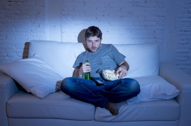 man sitting at home sofa in living room watching movie or sport in tv eating popcorn and drinking beer