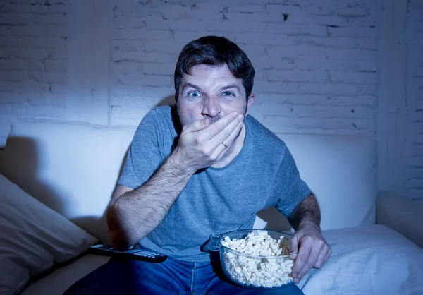 Joven atractivo hombre en casa acostado en el sofá en la sala de estar viendo la televisión comer palomitas de maíz crudamente tazón de espera —  Fotos de Stock