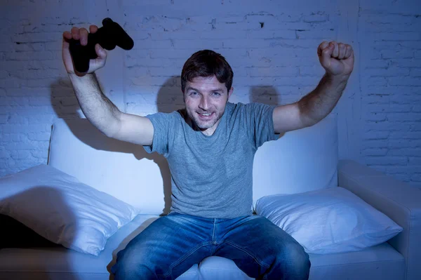 Jovem animado homem em casa sentado na sala de estar sofá jogando videogames usando controle remoto joystick — Fotografia de Stock
