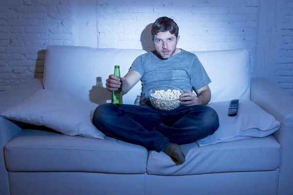 Homme assis à la maison canapé dans le salon regarder un film ou du sport à la télévision manger du maïs soufflé et boire de la bière — Photo