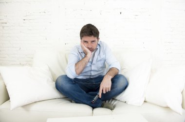 bored man watching television sitting on sofa holding remote control tired not having fun clipart