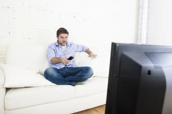 Молодой счастливый человек смотрит телевизор, сидя дома гостиная диван выглядит расслабленной наслаждаясь телевизором — стоковое фото