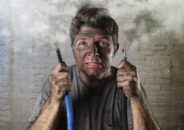 Необученный человек соединяющий электрический кабель страдает от электрической аварии с грязным обгорелым лицом в смешном выражении — стоковое фото