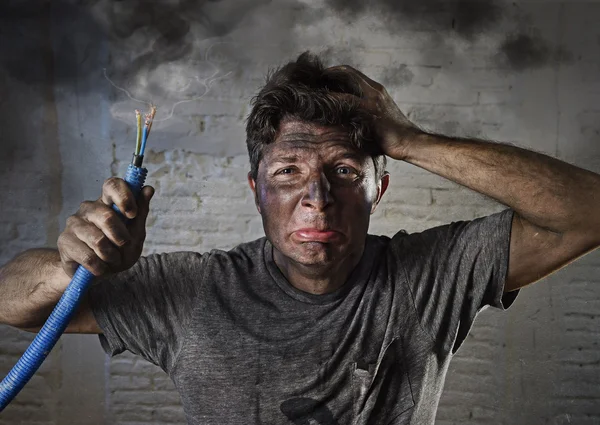 Giovane uomo che tiene il cavo di fumare dopo incidente elettrico con il viso sporco bruciato in divertente espressione triste — Foto Stock