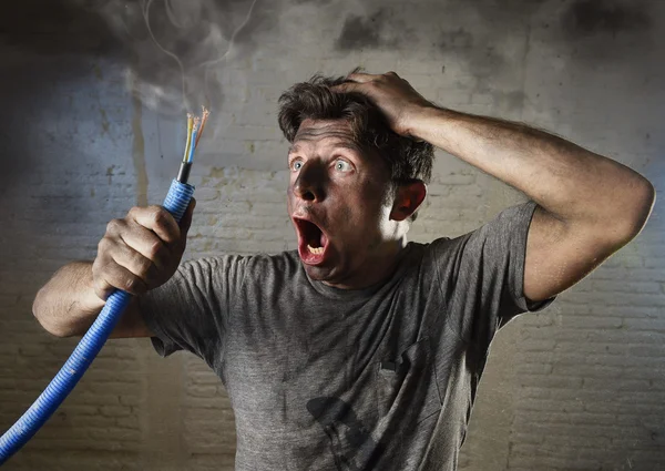 Young man holding cable smoking after electrical accident with dirty burnt face in funny sad expression — Stock Photo, Image