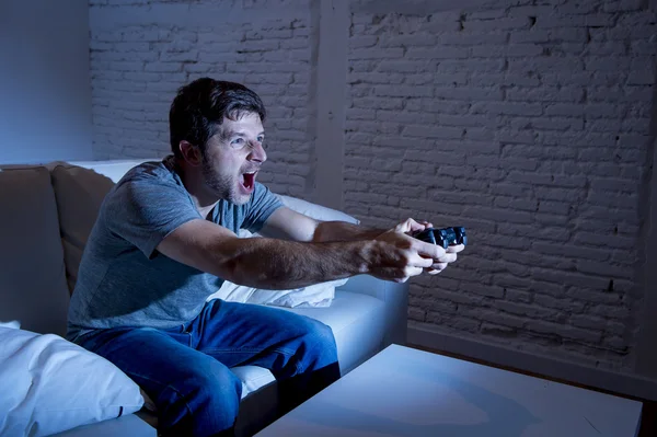 Junger aufgeregter Mann sitzt zu Hause auf Wohnzimmersofa und spielt Videospiele mit ferngesteuertem Joystick — Stockfoto