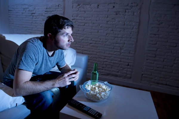 Joven adicto a la televisión hombre sentado en el sofá de casa viendo la televisión comer palomitas de maíz y beber botella de cerveza — Foto de Stock