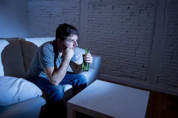 Jeune homme accro à la télévision assis sur le canapé à la maison regarder la télévision et boire une bouteille de bière regardant hypnotisé profiter d'un film sitcom ou de sport en direct la nuit — Photo