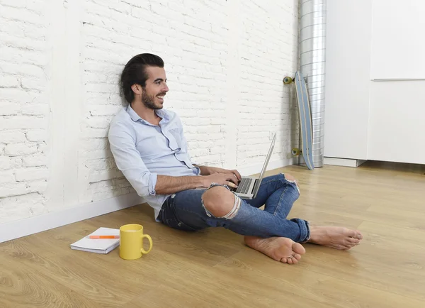 Young man in hipster modern casual style look sitting on living room home floor working on laptop — Stok fotoğraf