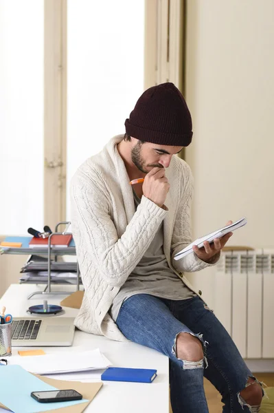 Hombre de negocios de moda en gorro hipster fresco y mirada informal escrito en almohadilla de trabajo en la oficina en casa — Foto de Stock