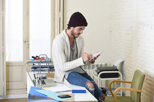 Hombre de negocios de moda en gorro hipster fresco y mirada informal escrito en almohadilla de trabajo en la oficina en casa — Foto de Stock